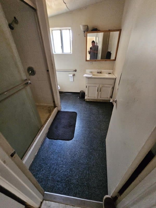 A dated bathroom — dark carpet, old vanity and shower — before its accessible remodel by RLS Custom Carpentry in Mendocino County, CA