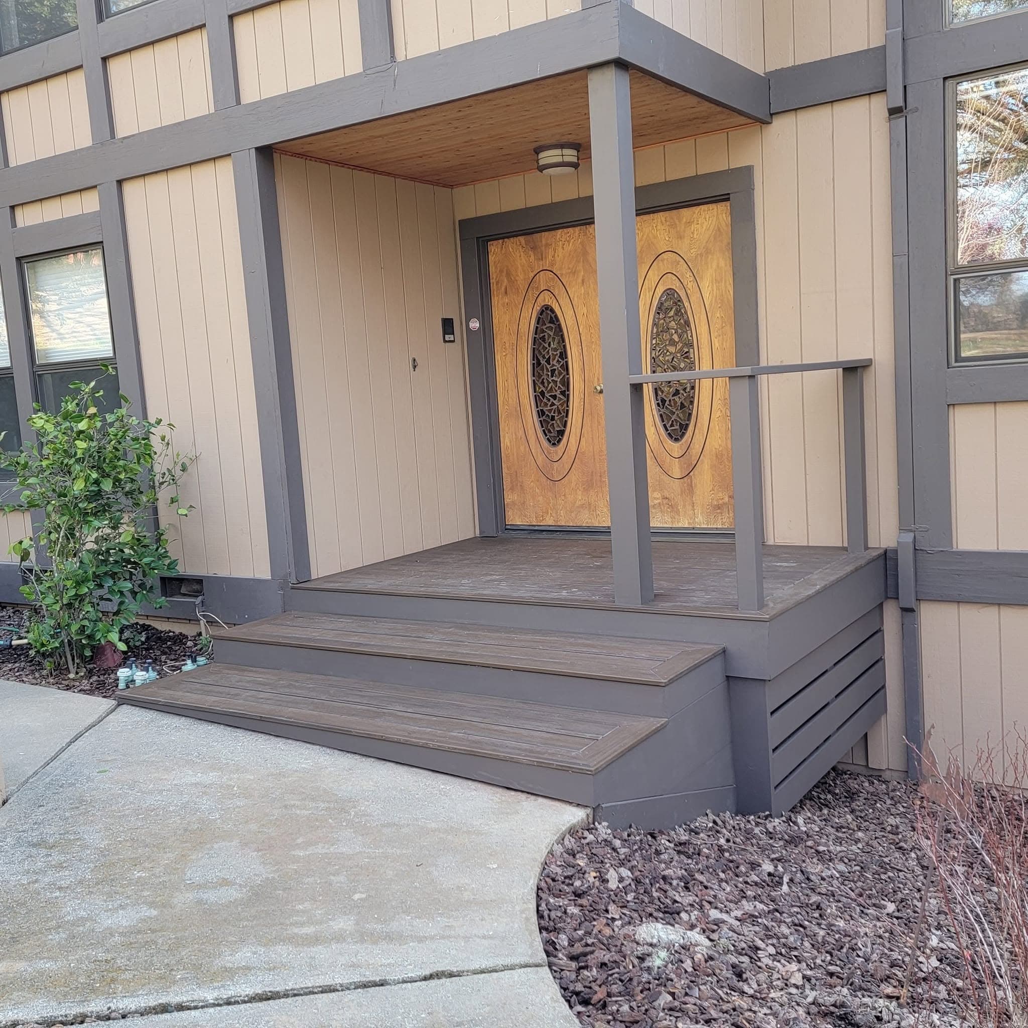 Custom front entry remodel featuring carved wood double doors, gray board-and-batten siding, and a composite deck porch with steps by RLS Custom Carpentry in Mendocino County, CA
