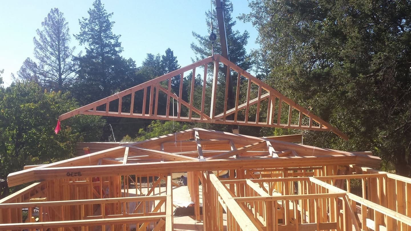 Crane lifting a prefabricated roof truss into place on a wood-framed building under construction, structural framing project by RLS Custom Carpentry, Mendocino County CA