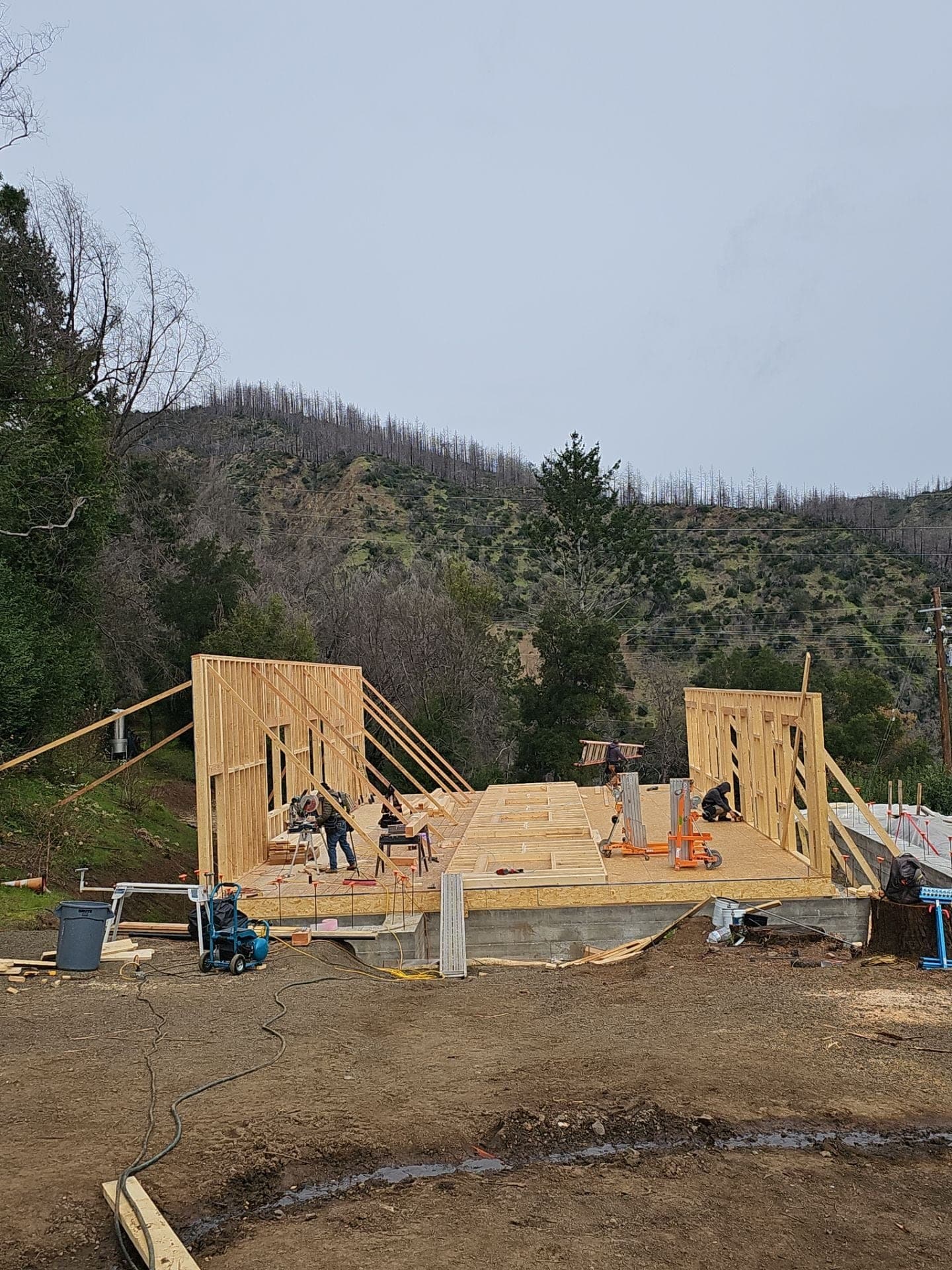 RLS Custom Carpentry crew framing and raising exterior walls on a new-home subfloor deck against a hillside in Mendocino County, CA