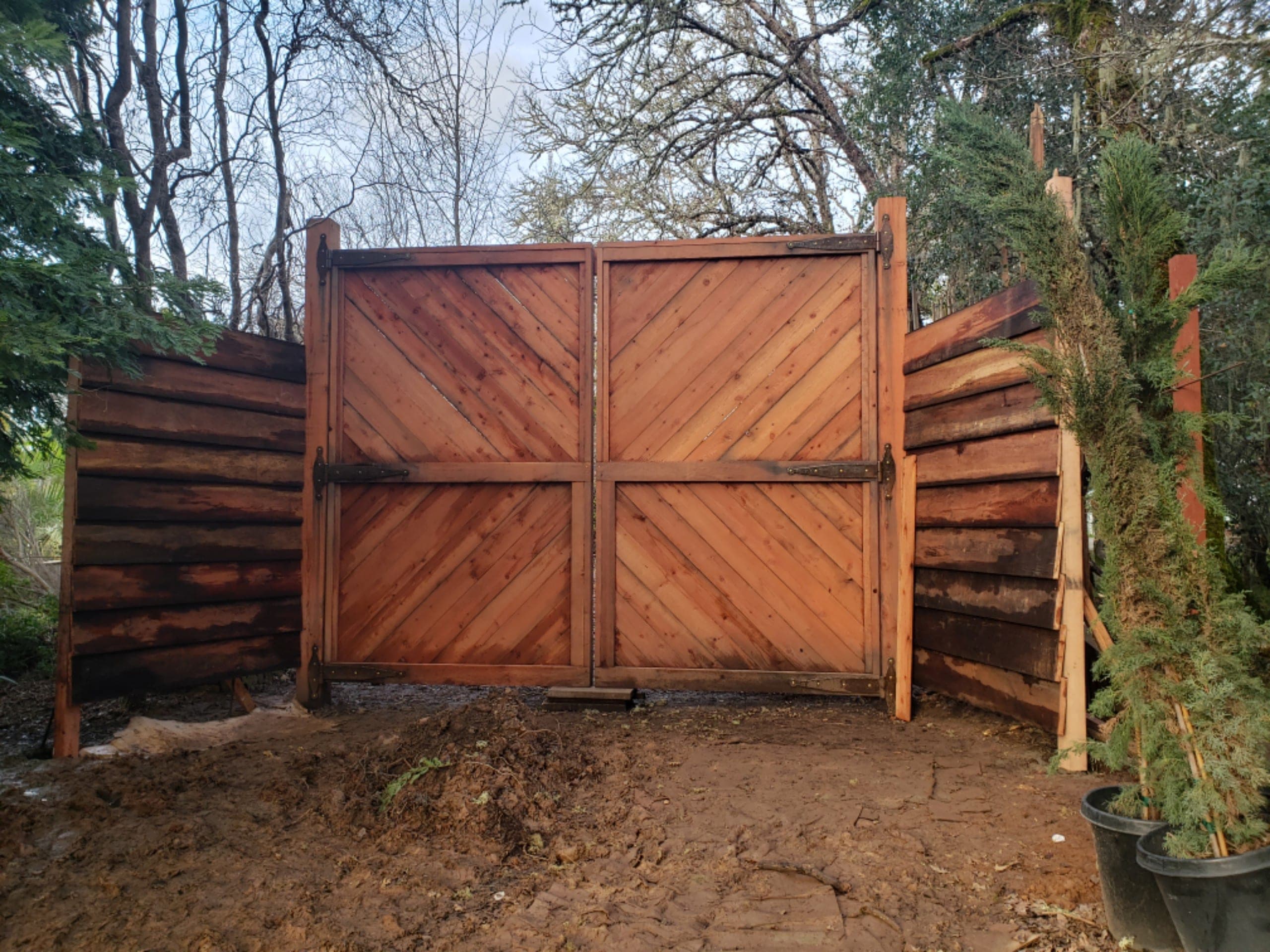 Huge custom redwood diagonal-batten gate built by RLS Custom Carpentry against a bare-winter treeline in Mendocino County, CA