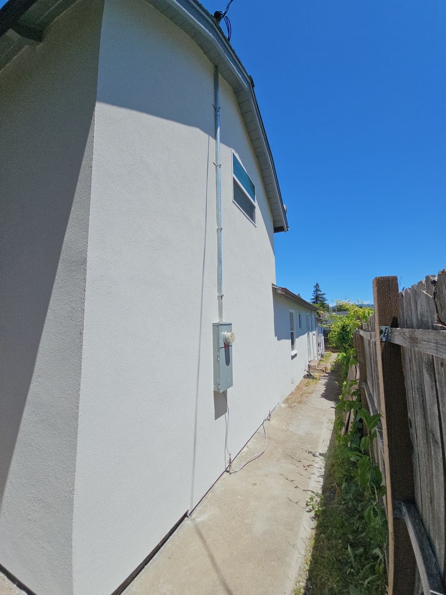 Newly finished white stucco exterior wall and side-yard pathway on a Mendocino County home remodeled by RLS Custom Carpentry