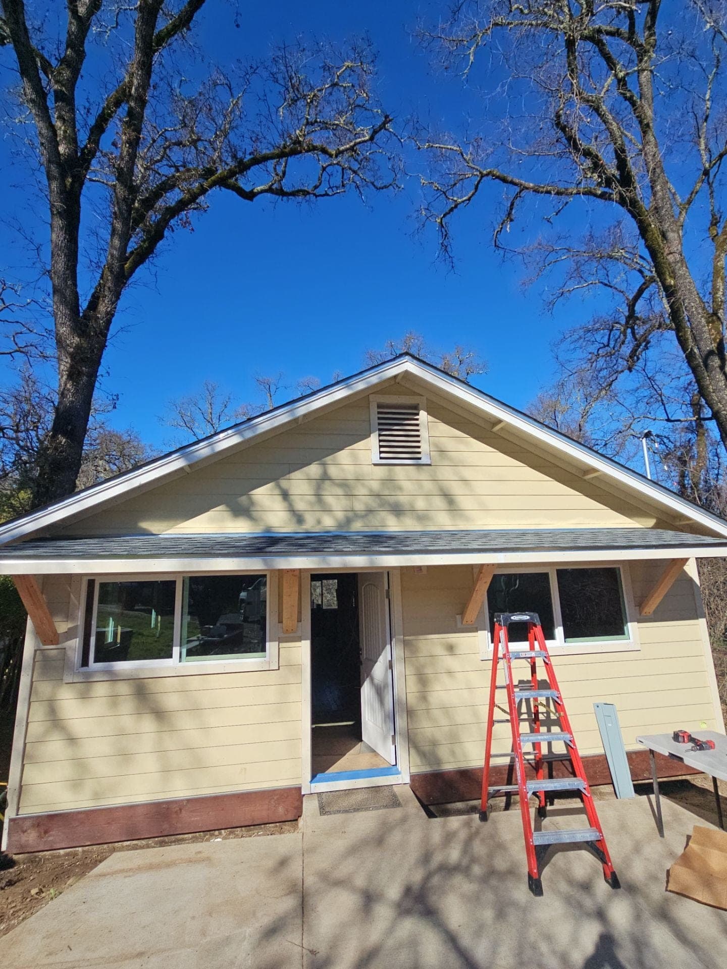 Remodeled yellow bungalow front with new windows, lap siding and decorative eave brackets at 5160 Burke Hill Rd in Mendocino County by RLS Custom Carpentry