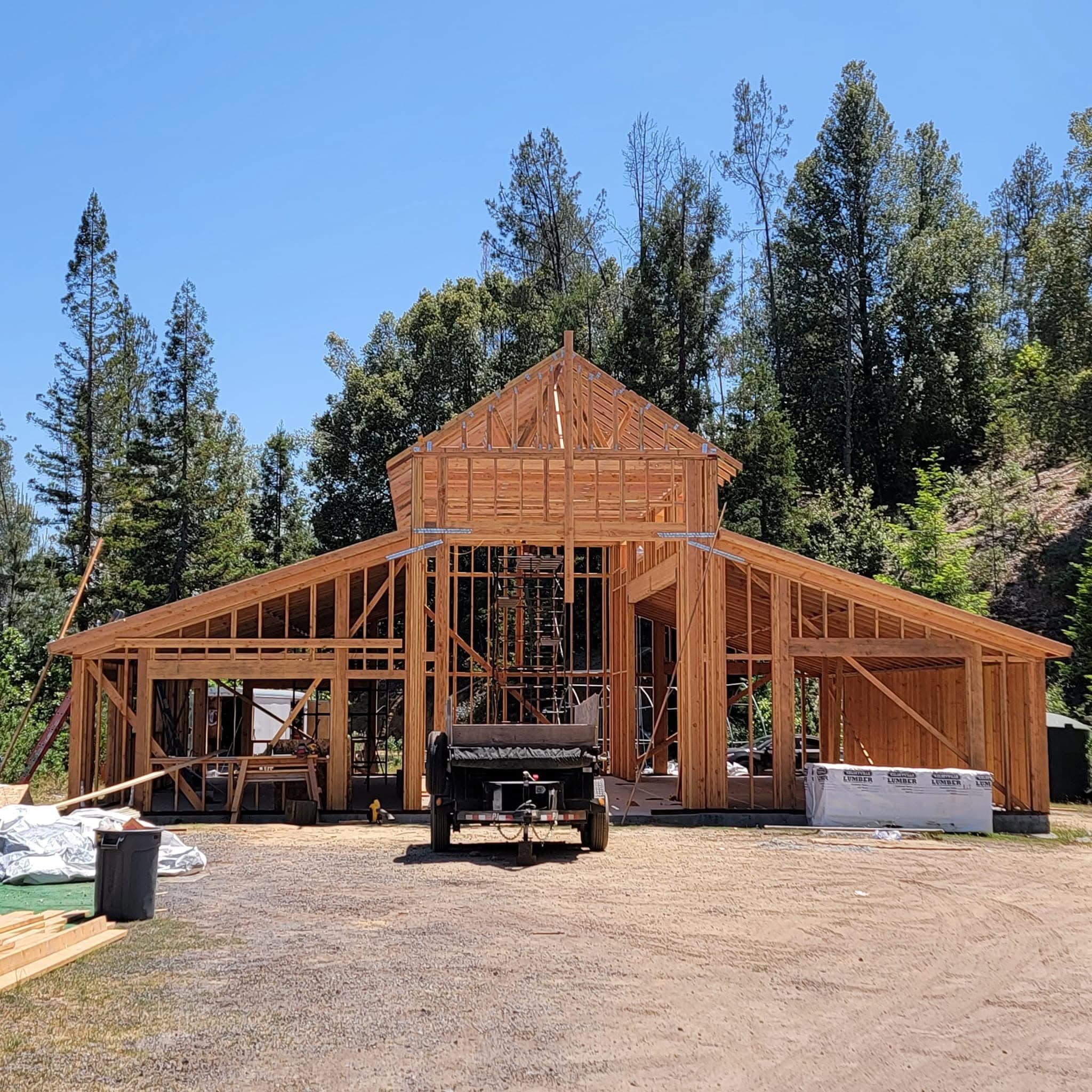 Large barn-style building framed in dimensional lumber with a center gable cupola and roof trusses, set against a pine forest in Mendocino County, CA, framed by RLS Custom Carpentry