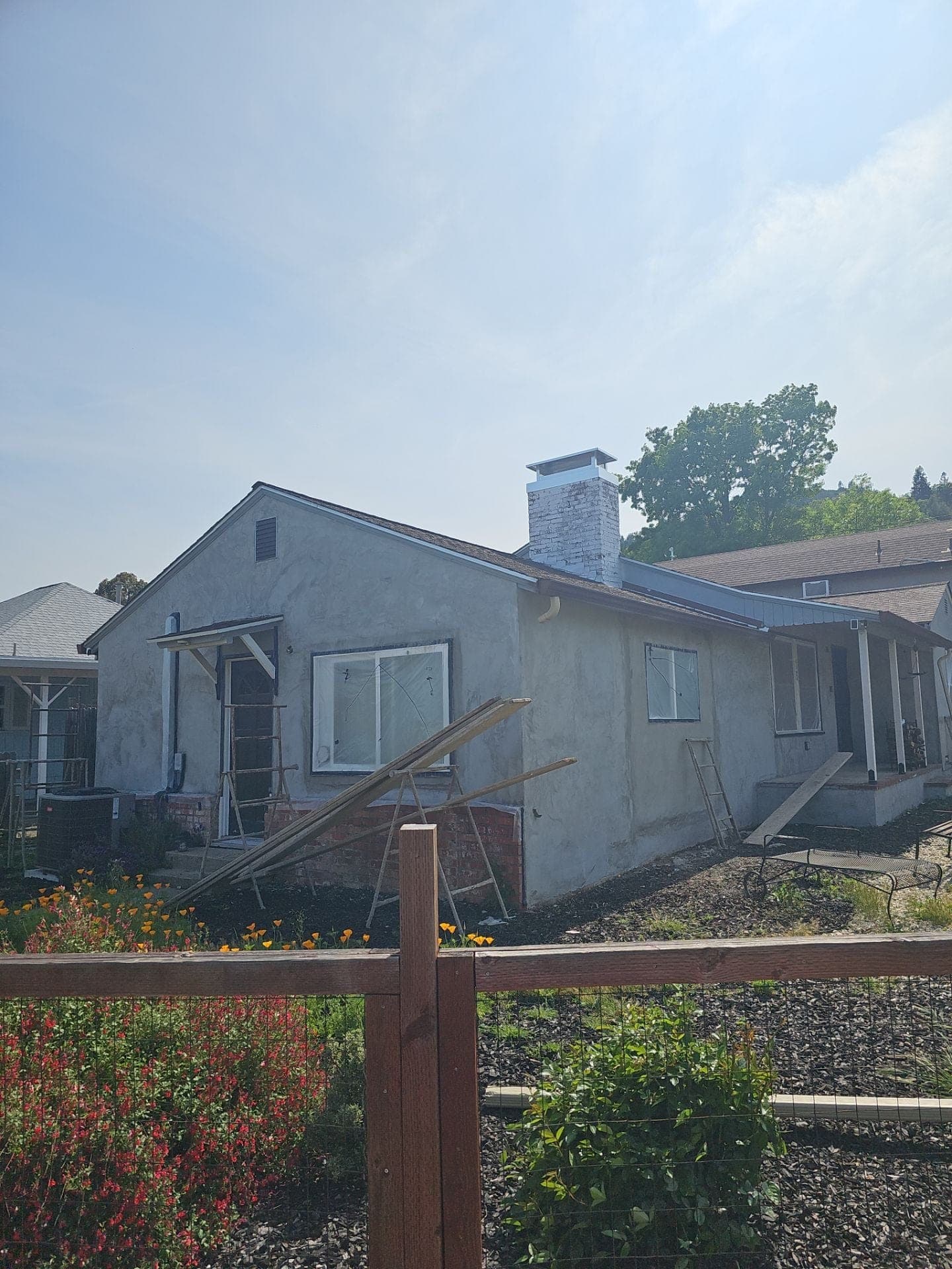 Rear of the original single-story house with new stucco scratch coat, brick chimney and work ladders during a whole-home remodel by RLS Custom Carpentry in Mendocino County, CA