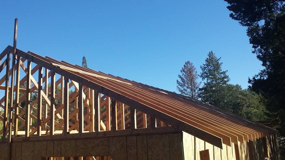 Roof rafter and truss framing in progress against a clear blue sky with OSB wall sheathing, structural framing by RLS Custom Carpentry in Mendocino County CA