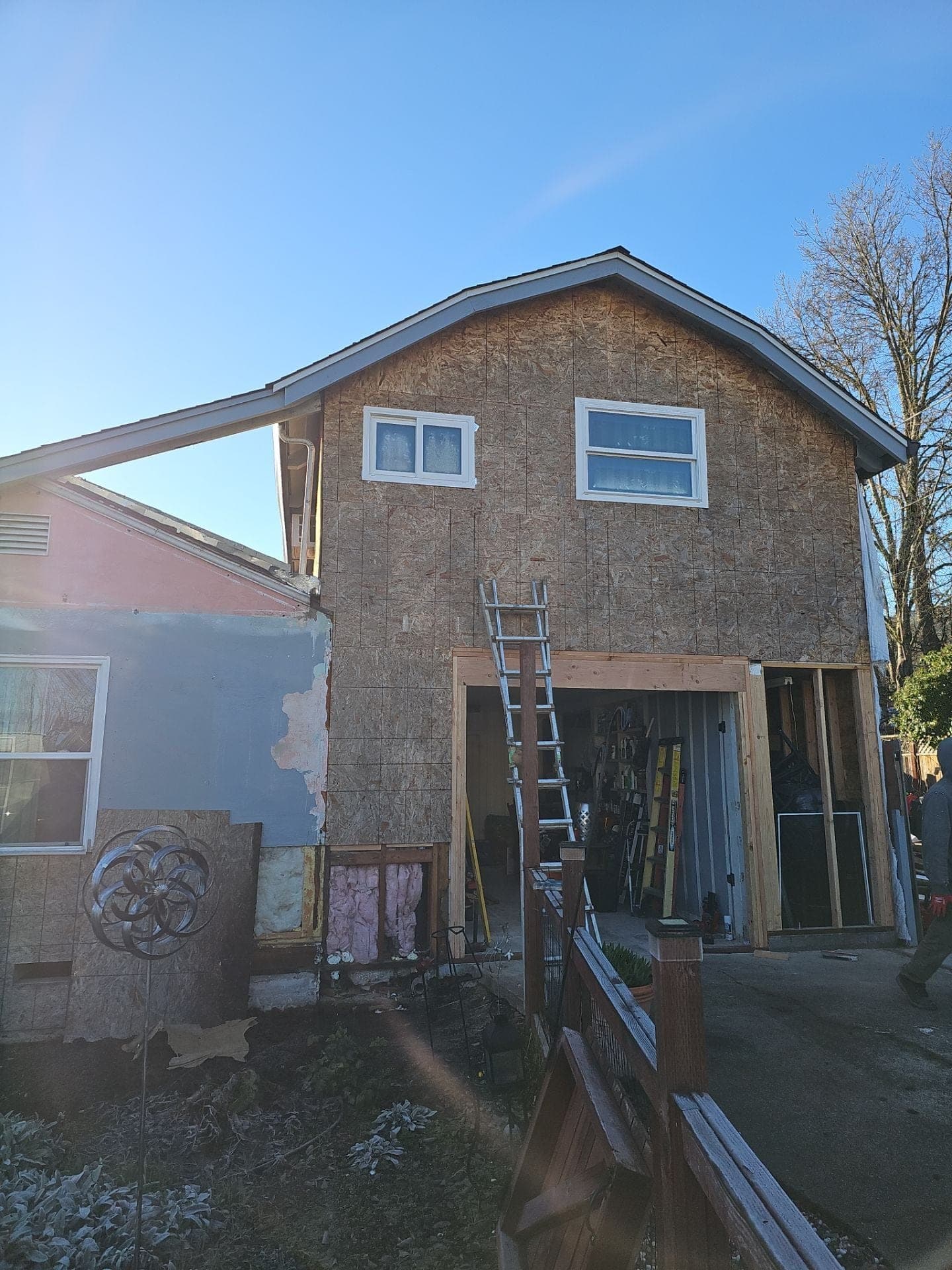 Two-story home addition in progress at 15 Mill Ct in Mendocino County, showing exposed OSB sheathing, new windows, and a framed garage opening by RLS Custom Carpentry