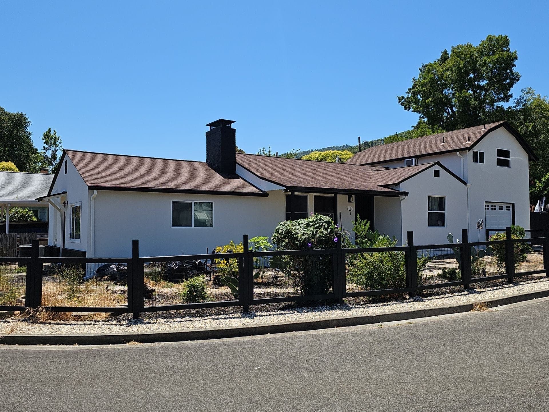 Wide street view of a remodeled white stucco home with brown roof, attached garage, and custom black wood fencing completed by RLS Custom Carpentry in Mendocino County, CA